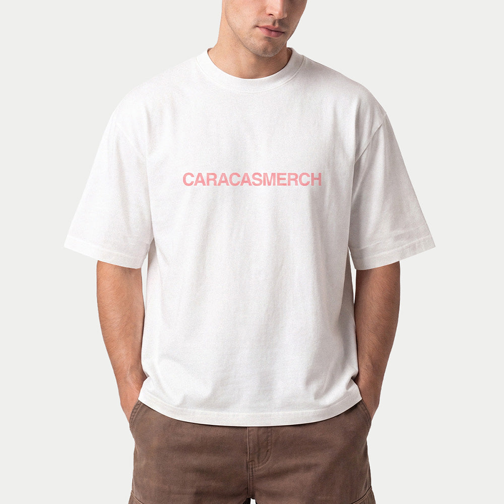 Man wearing the white Caracasmerch boxy t-shirt with the pink chest wordmark and brown trousers